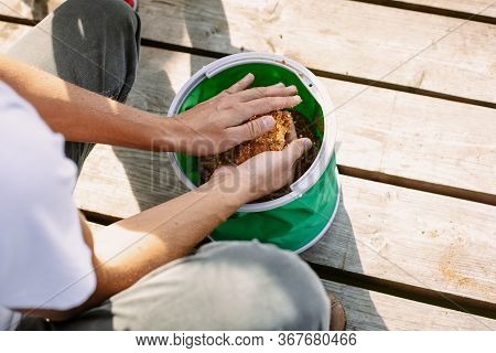 The Fisherman Picks Up The Bait For The Fish From The Bag. Hands Close Up