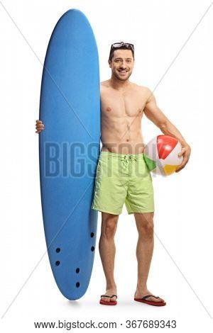Full length portrait of a young man with a surfboard standing and holding a bech ball isolated on white background
