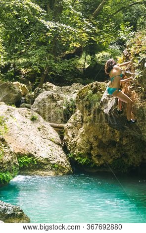 A Woman In A Swimsuit Climbs A Cliff Above The Water, Climbing Over A Mountain River, Bouldering In 