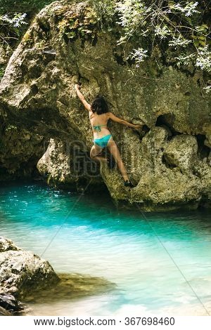 A Woman In A Swimsuit Climbs A Cliff Above The Water, Climbing Over A Mountain River, Bouldering In 