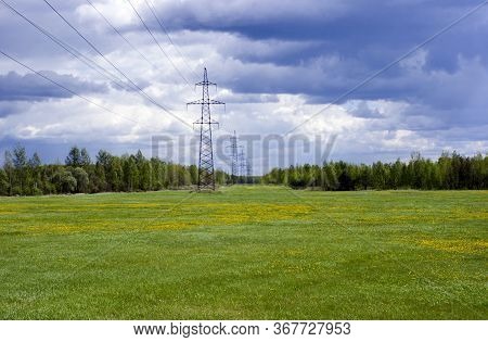 Landscape With Green Field And Forest In The Distance With Electric Power Poles Extending To The Hor
