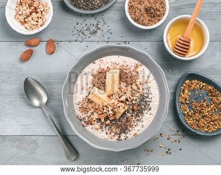 Overnight Oats In Bowl And Ingredients - Banana, Lsa, Chia Seeds, Almond, Honey And Pollen On Gray W