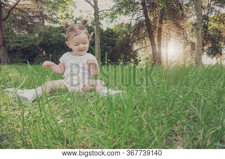 Baby Girl Sitting In Grass In Park Touching Playing And Exploring Nature - Cute Kid Toodler Outside 