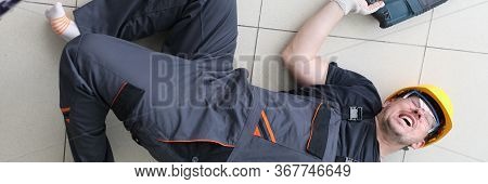 Severe Pain In Back Builder, Man Lies On Floor. Man In Work Clothes And Helmet Lies On Floor With Wr