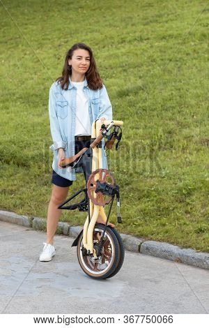 A Beautiful Young Woman Folds Up And Unfolds A Bicycle. Convenient Folding Bike For Travel And Trans