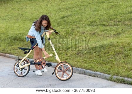 A Beautiful Young Woman Folds Up And Unfolds A Bicycle. Convenient Folding Bike For Travel And Trans
