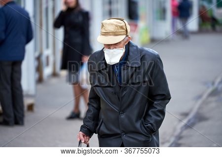 An Old Grandfather Wearing A Medical Mask, With A Cake In His Hands Asking For Money. A Beggar Near 