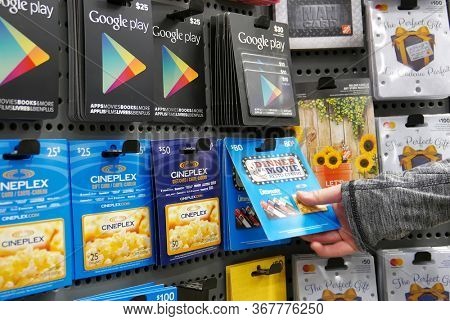 Port Coquitlam, BC, Canada - September 15, 2017 : Motion of woman picking cineplex fifty and eighty dollar gift cards inside Home depot store