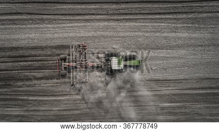 Aerial View Of A Clean Field In Which The Tractor Makes Vertical Tillage. Red Tillage Equipment And 