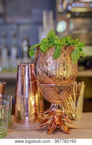 Gold Metallic Cup With Mint And Shaker In The Background On Bar