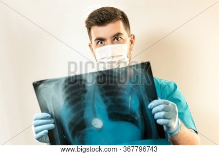 Young Male Doctor In A Mask From A Virus, Examines An X-ray.
