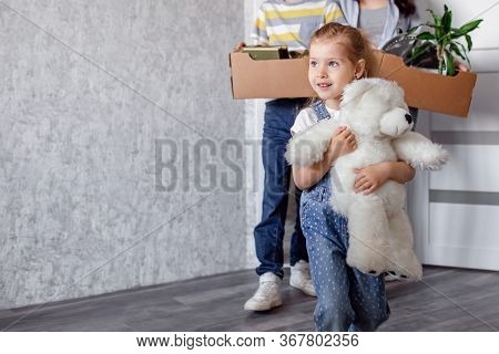 The Family Moves Into A New Apartment, A Little Girl Runs In The Door, Holding Cardboard Boxes In Th