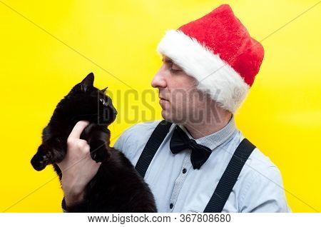 Handsome Man In Red Santa Hat, Blue Long Sleeve Shirt Holding,  Hugging And Looking At Cute Black Ca