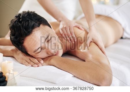 Masseuse Giving Deep Tissue Back And Shoulder Massage To Young Man