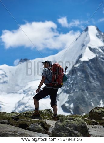 Zinal, Switzerland - July 19, 2019: Male Traveler With Backpack Holding Bottle Of Water And Looking 