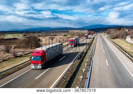 Fleet Of Red Trucks In Line As A Convoy At A Rural Countryside Highway Under A Beautiful Blue Sky