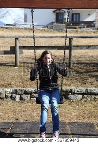 Beautiful Young Caucasian Girl With Long Hair Plays On The Swing In The Outdoor Playground