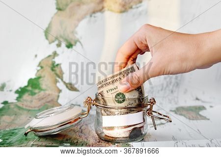 Collecting Money For Travel. Hand With Coin, Money Box With Dollar Banknotes. Cash Savings In Glass 