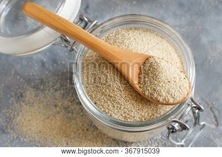Raw Uncooked Fonio Seeds In A Glass Jar With A Spoon On Grey Background Close Up