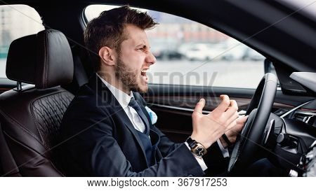 Angry Driver Concept. Aggressive Mad Man In Suit Driving Car In Urban City, Angrily Gesturing