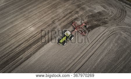 Aerial View Of A Clean Field In Which The Tractor Makes Vertical Tillage. Red Tillage Equipment And 