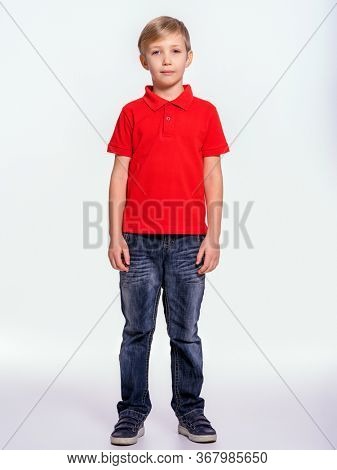 Young pretty boy posing at studio as a fashion model. Photo of a 8 years old kid. Full portrait of boy, isolated.  Portrait of white kid in a red t-shirt and jeans. Boy in a full length