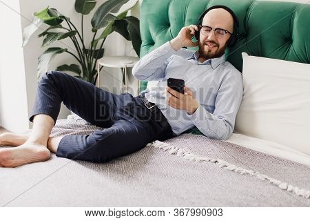 Young Man Lying On Bed At Home, Listening To Music Through Headphones Eyes Closed.