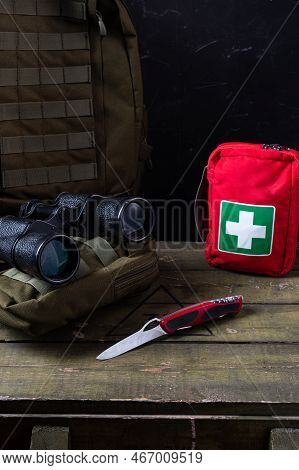Swiss Army Knife And First Aid Kit. Binoculars And Military Backpack On A Military Box. Vertical Fra