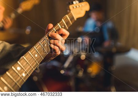 Unrecognizable Human Hand Touching Neck And Strings Of Professional Guitar. Blurred Band Members In 