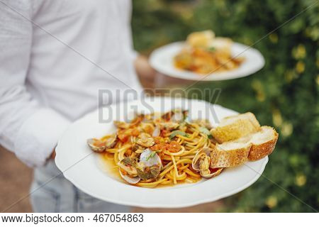 Seafood Spaghetti With Seashells, Prawns, Squids Hands Of The Waiter On Ature Background. Italian Me
