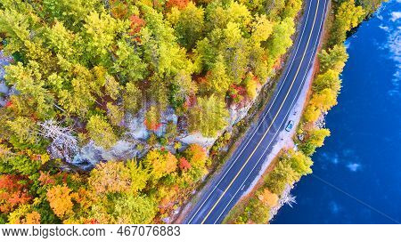 Aerial Looking Down On Road Next To Lake And Surrounded By Fall Foliage And Rocks