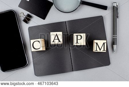 Word Capm On Wooden Block On A Black Notebook With Smartpone, Credit Card And Magnifier