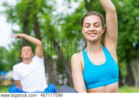 Young Couple Doing Yoga In Park Together. Man And Woman Sitting In Yoga Pose On Green Grass. Trainin