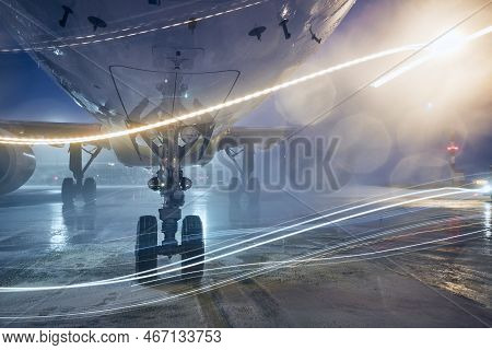 Airplane Landing Gear During The De-icing Process. Winter Night At Airport During Snowfall.
