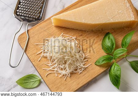 Grated Grana Padano Cheese On A Cutting Board. Italian Parmesan Cheese Wedge And Grated, Hand Grater