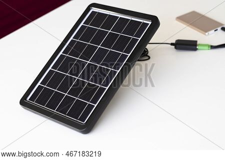 A Small Solar Panel On A White Background Charges A Paverbank.