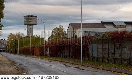The Site Of The Former Steelworks. Asphalt Street With Lampposts, Old Wall (overgrown With Wild Vine