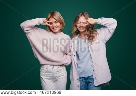 Photo Of Pretty Two Women Showing V-sign Symbols Looking At Camera Isolated Over Green Color Backgro