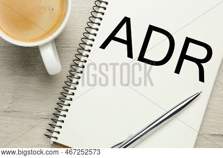 Alternative Dispute Resolution. Notebook With Abbreviation Adr, Pen And Cup Of Coffee On Wooden Tabl