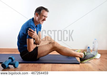 Man Doing Sports Indoors Complaining Of Shoulder Pain Sitting On A Mat. Side View