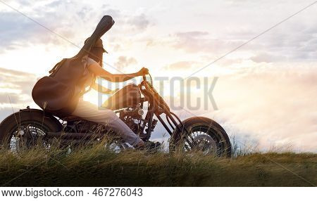 Guitarist Woman Riding A Motorcycle On The Countryside Road, Sunset Background