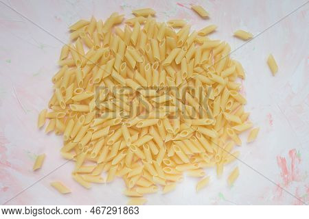 Pile Of Raw Traditional Italian Penne Pasta On Piink Background. Ingredient For Cooking. Closeup, To