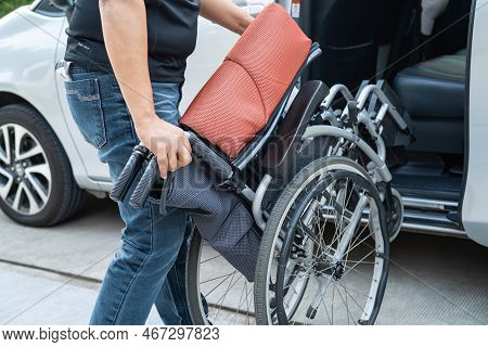 Asian Woman Folding And Lift Up Wheelchair Into Her Car. Accessibility Concept.
