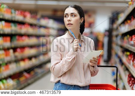 Shopping Concept. Portrait Of Young Thougtful Caucasian Woman Choosing Groceries In Supermarket. Mil