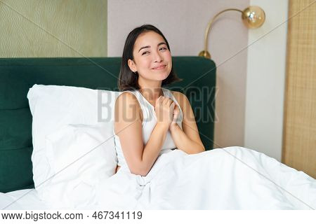 Portrait Of Excited, Smiling Asian Woman Sitting In Her Bed In Morning, Daydreaming, Looking Hopeful