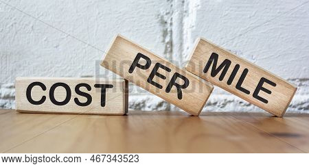 Cost Per Miles Text On Wood Block, White Brick Wall Background