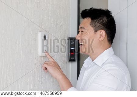Close-up Photo. A Young Asian Man Rings An Electronic Doorbell On The Wall Of A House With His Finge