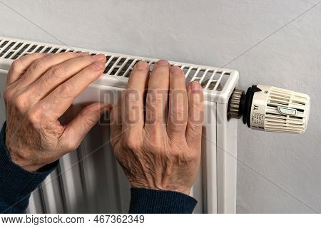 Elderly Man's Hands Trying To Keep Warm On The Heating Radiator. Close Up.