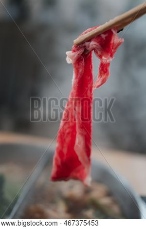 Hand Using Chopsticks Pick Raw Fresh Beef Over The Hot Pot Soup For Shabu Shabu Dipping And Dropping