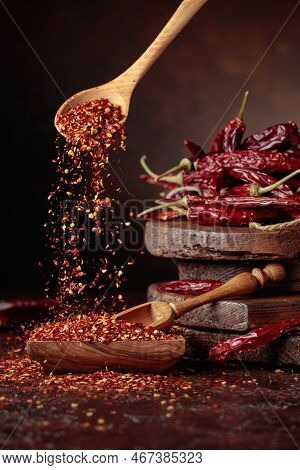 Chilli Flakes Are Poured Into A Wooden Dish. Chilli Flakes And Dried Chili Peppers On A Brown Backgr